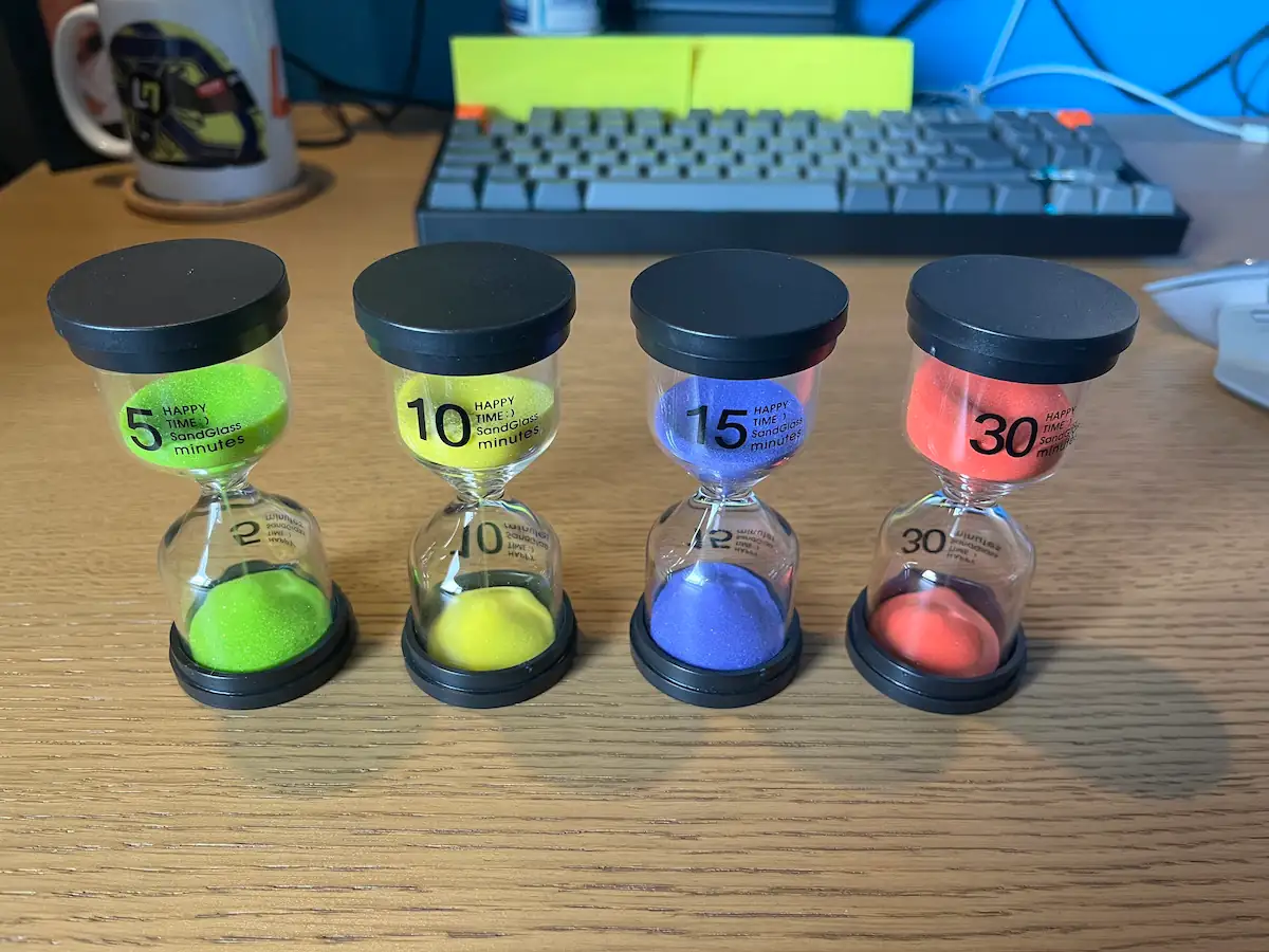 4 sand timers on a desk with a mouse and keyboard in the background. 